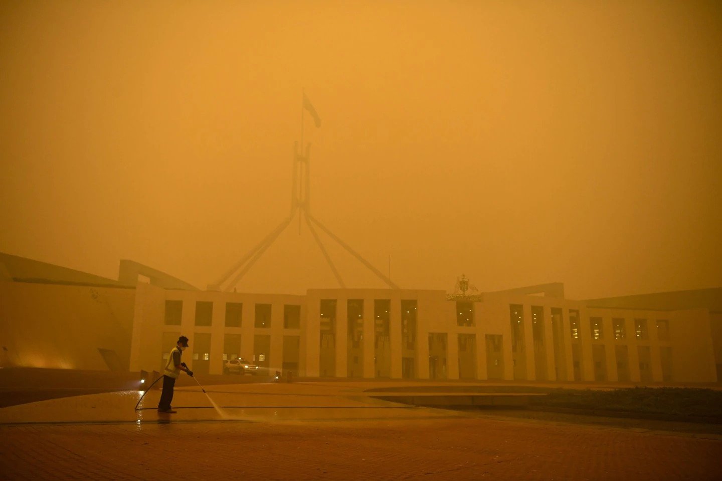 Amid an early-morning smoky haze, a man cleans the forecourt of Parliament House in Canberra, Australia, on Jan. 5. (Lukas Coch/Reuters)